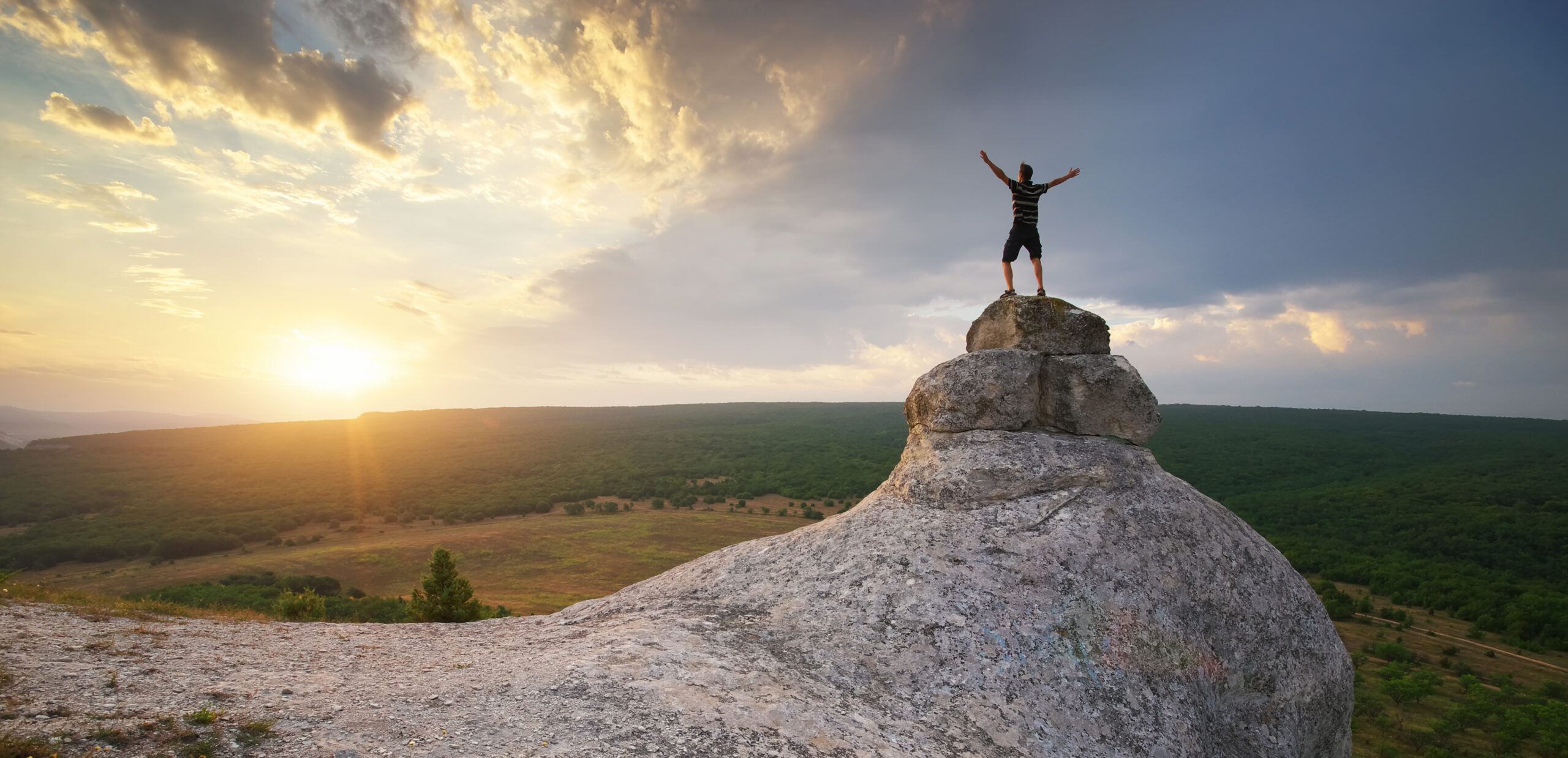 Seminar Positive Psychologie Mann auf Felsen streckt Arme gegen Himmel Sonnenaufgang